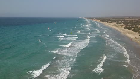 Aerial-rises-as-kite-surfers-crowd-windy,-shallow-sand-beach-on-Kos