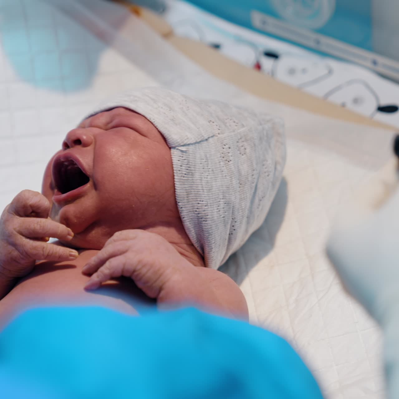 Medic's hands in latex gloves clean the face of newborn with a napkin. The doctor cutting the umbilical cord
