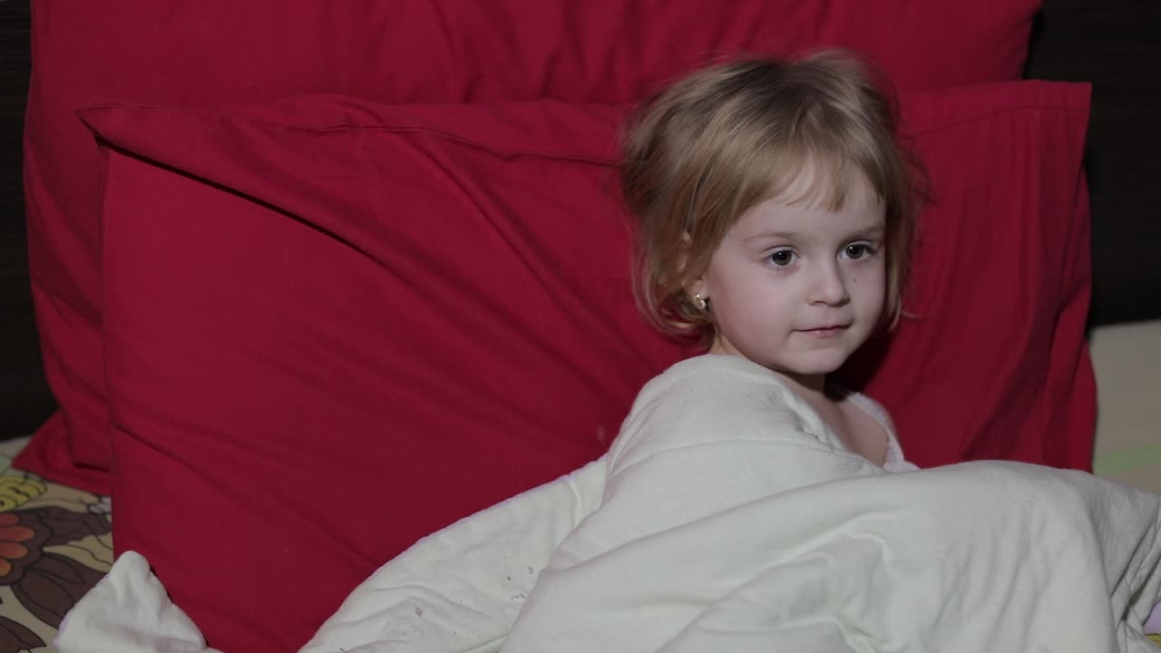 어린 소녀가 침대에 앉아 tv를 보고 있다.