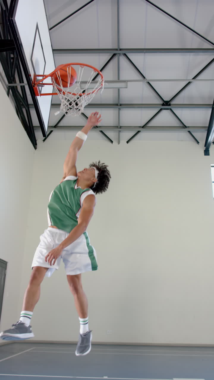 Vertical video: Dunking basketball, male athlete in green jersey jumping high in gym
