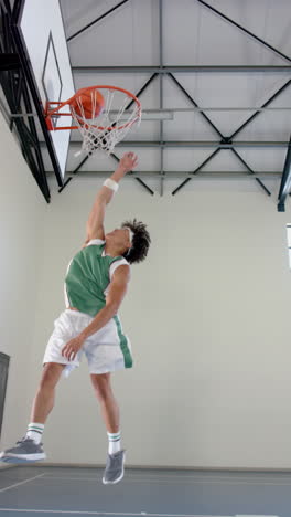 vertical video: dunking basketball, male athlete in green jersey jumping high in gym