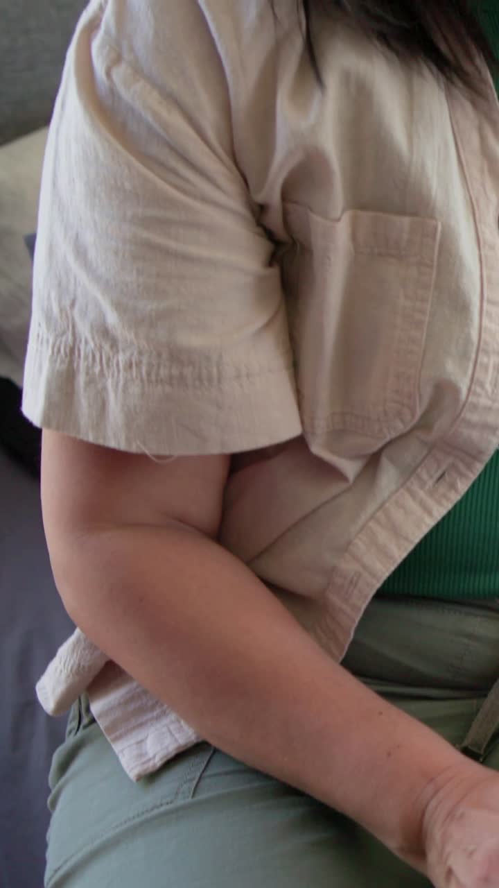 Vertical video: Shifting woman hand resting in green pants on sofa placing finger on white reader
