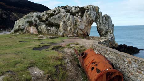 Red-rusty-industrial-mill-tank-abandoned-on-scenic-Anglesey-rocky-archway-coastline