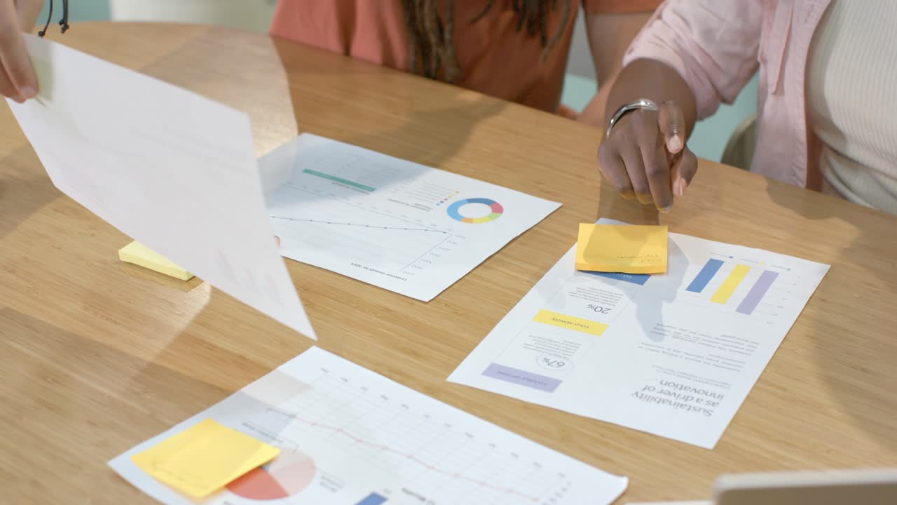 Left woman reaching at table is starting; right woman pressing notes and sorting charts for review