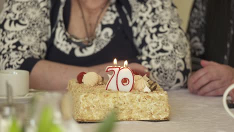 senior woman blowing out candles on birthday cake at dinner table