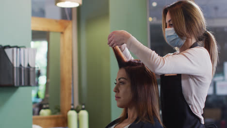peluquera que usa una máscara facial poniendo rodillos en el cabello de una cliente femenina en una peluquería