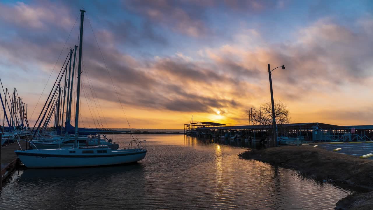 los barcos atracados en la roca del muelle mientras las nubes pasan sobre el amanecer dorado que se refleja en el agua