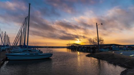 boats moored at dock rock as clouds pass over golden sunrise reflecting on water