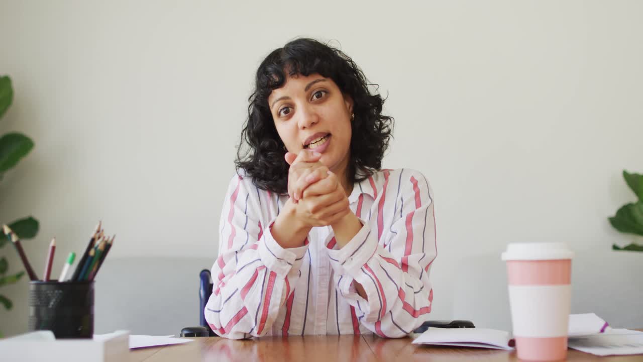 feliz mujer biracial sentada en el escritorio hablando y gestando durante una llamada de video