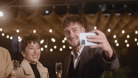 portrait of group of four happy multiethnic friends taking a selfie video and toasting with champagne glasses at new year's eve party 1