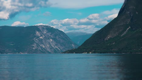 Panoramic-shot-of-a-serene-fjord-surrounded-by-steep,-rugged-mountains-under-a-partly-cloudy-sky