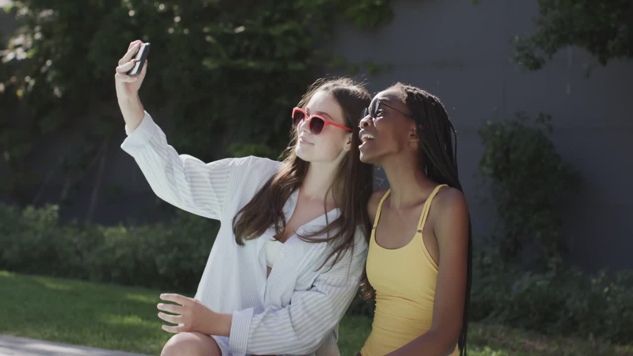 diversas amigas adolescentes felices con gafas de sol tomando selfies en el jardín en cámara lenta