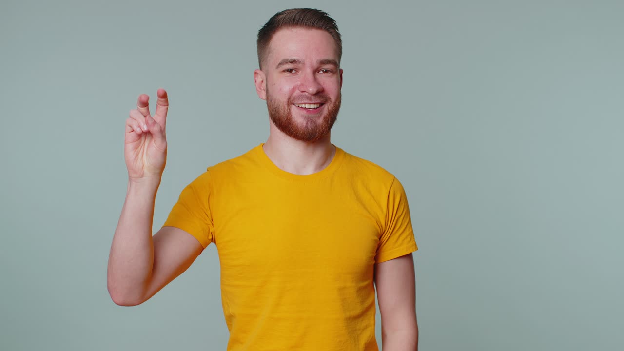 잘생긴 즐거운 미소 짓는 남자가 승리의 표시를 보여주고, 성공과 승리를 희망하며, 평화의 제스처를 하고 있습니다.