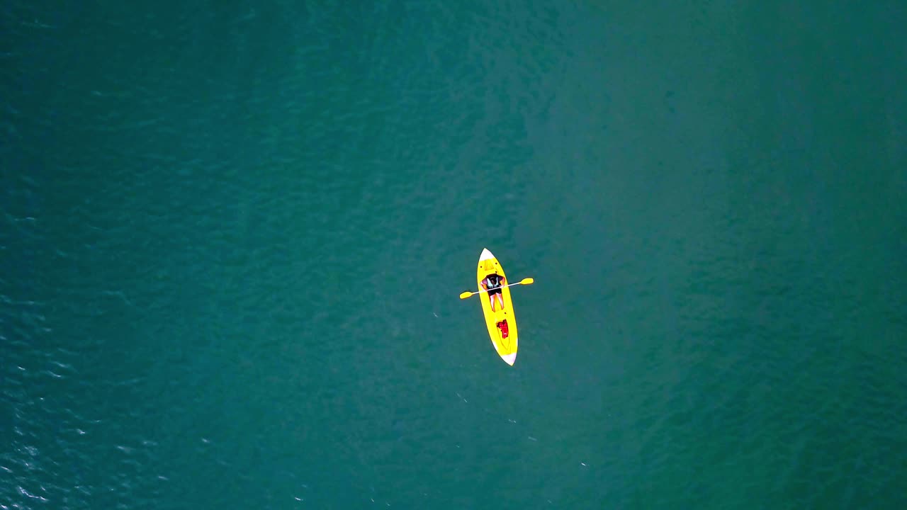 Aerial top down shot of an unrecognizable man rowing against current at the sea