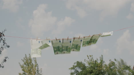 Several-banknotes-of-one-hundred-euros-are-drying-on-a-clothesline.-Money-laundering-concept.-Low-angle-shot