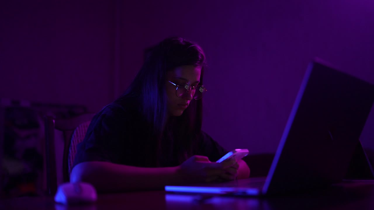 Young Woman Working on Laptop and Phone at Night