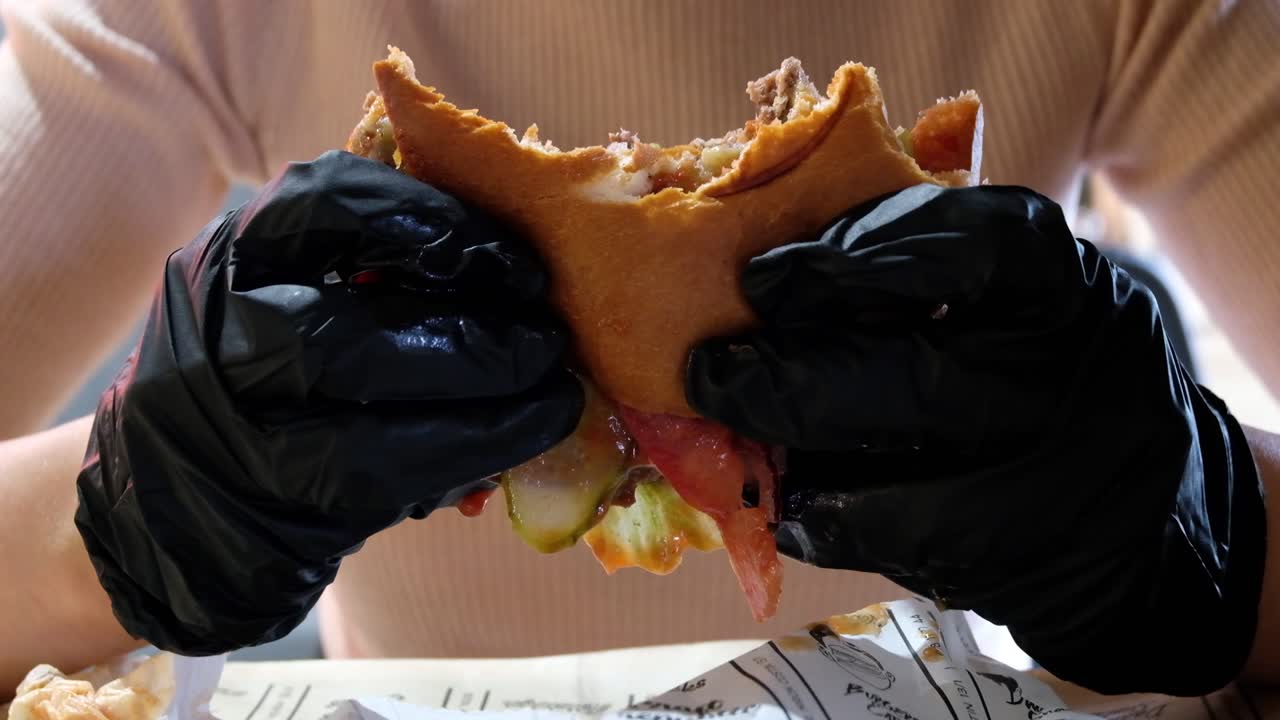 Close up of a woman with black gloves eating a hamburger in a restaurant