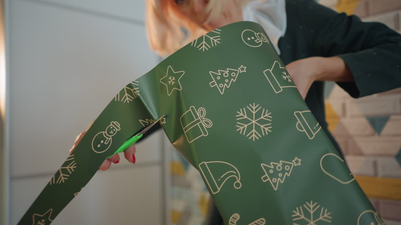 White blonde woman wrapping Christmas present, trimming paper with scissors, tying ribbon bow, smoothing edges, arranging box on table, smiling while preparing intimate holiday gift in warm room