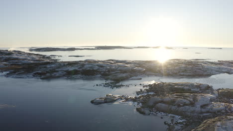 drone shot of gothenburg archipelago, sweden. a small wooden house can be seen on a small rocky island during sunset.