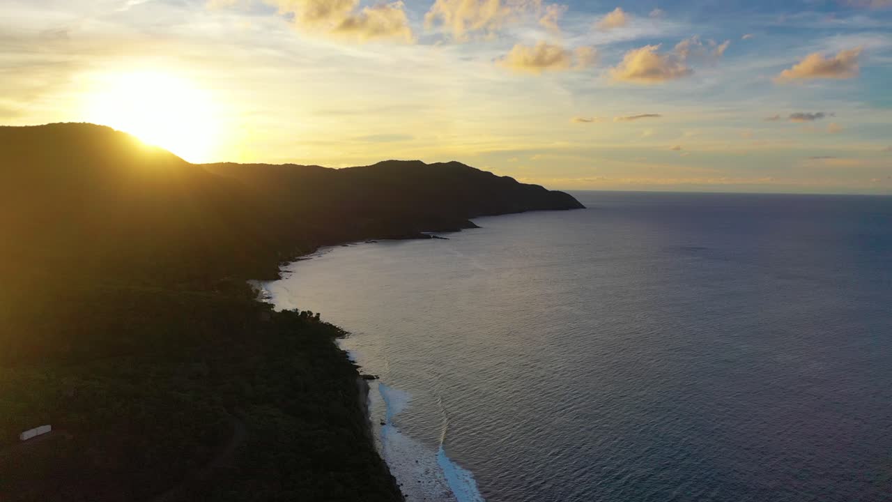 Scenic sunrise over St. Croix’s shoreline, with waves glimmering in the early light, palm trees rustling gently, and the peninsula glowing beneath a vivid sky