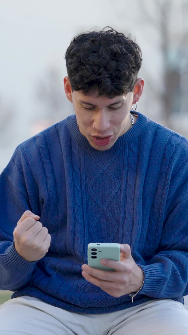 Young man celebrating success on smartphone. Vertical