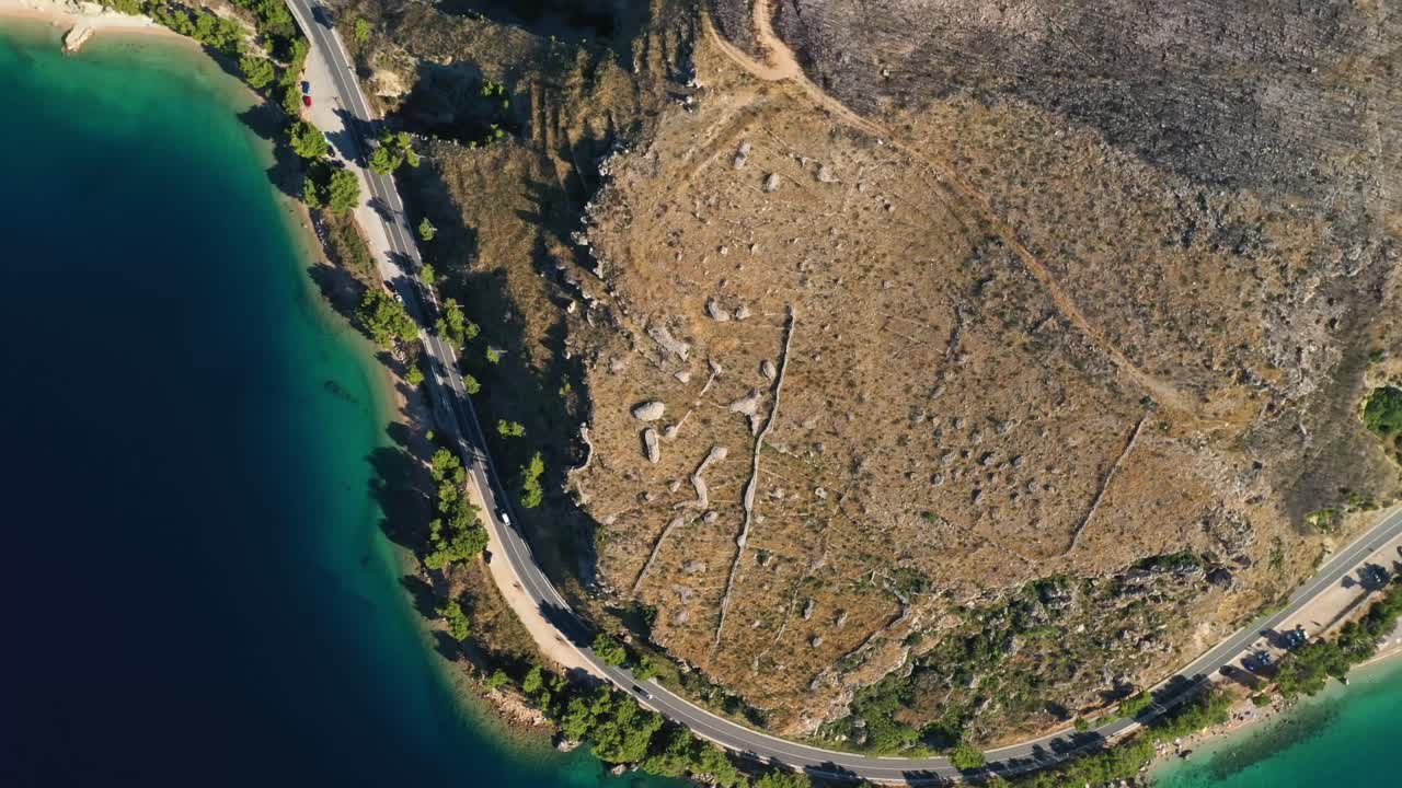 수정처럼 맑은 물이 있는 아름다운 만을 따라 반도의 해안 도로를 주행하는 자동차의 공중 회전 드론 영상