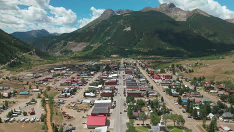 drone aéreo cinematográfico mañana de verano en el centro de silverton calle principal sur de colorado paso de la montaña roja impresionante verde exuberante cielo azul parcialmente nublado montañas rocosas movimiento hacia adelante de la ciudad