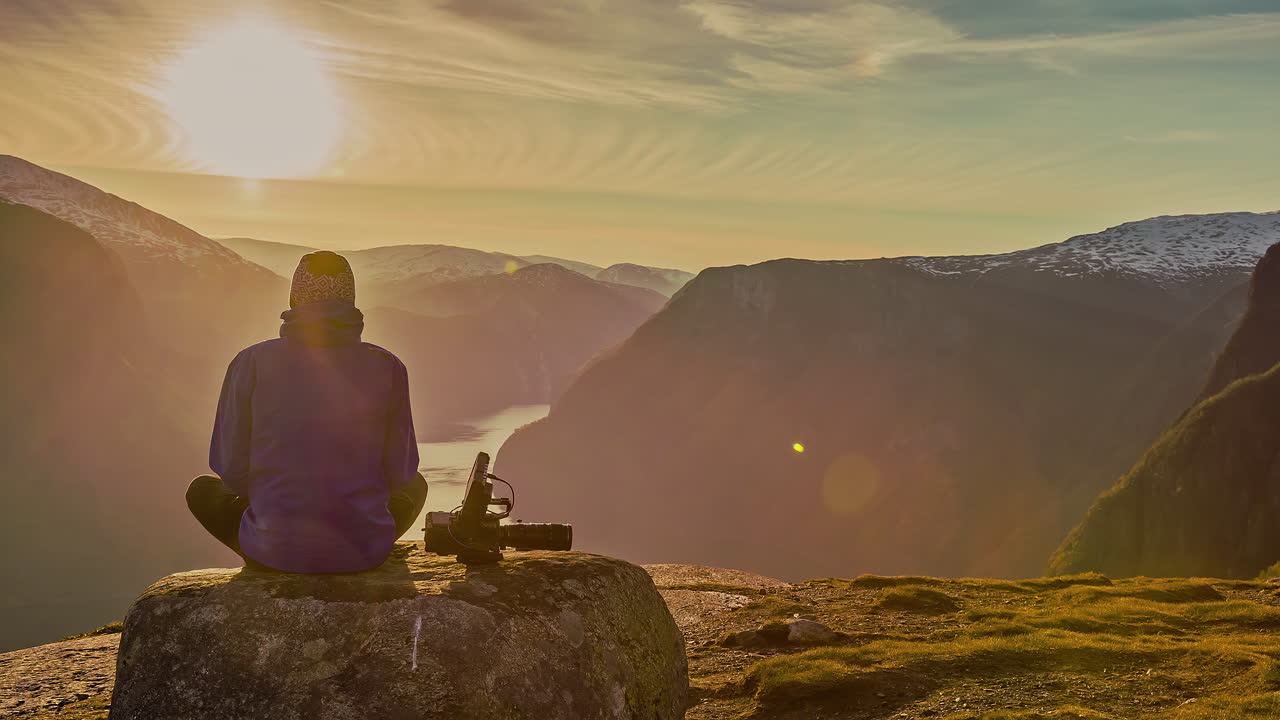 tiro de lapso de tiempo con un tipo sentado en una roca y mirando la cordillera en noruega al atardecer