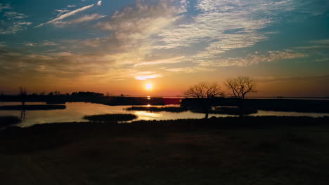 Crane-shot-moving-up-to-reveal-a-peaceful-sunset-over-still-lake,-reflecting-a-teal-and-orange-sky