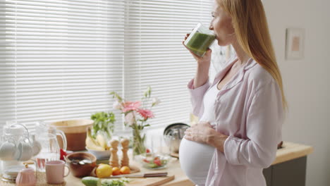 pregnant woman drinking smoothie in kitchen