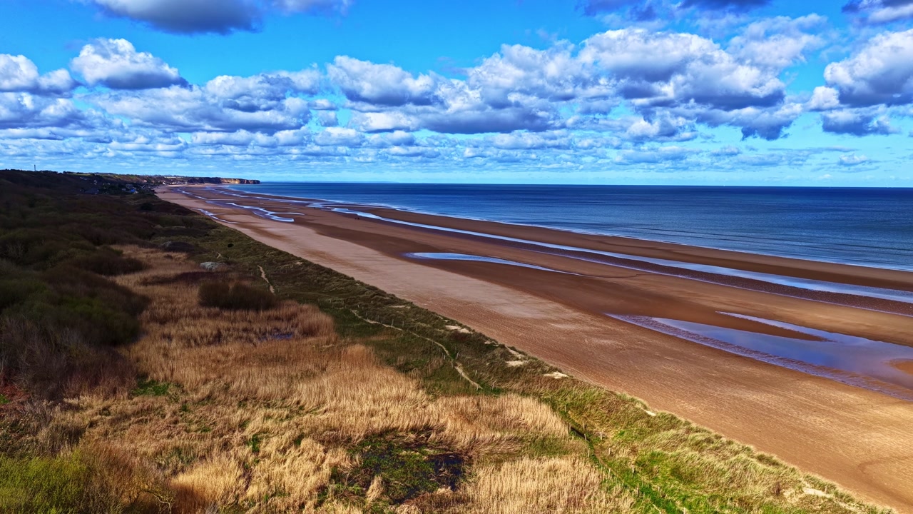 Aerial drone flyover reveals vast empty golden sands of Omaha Beach, historic WWII D-Day landing site with dunes and English Channel in Normandy, France