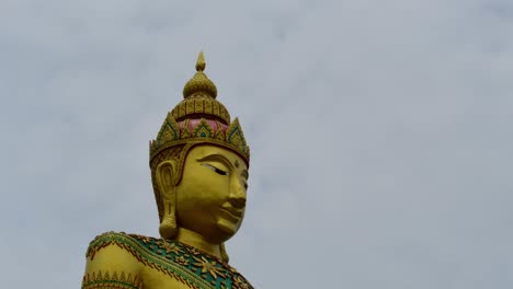 dolly out primer plano de la hermosa escultura dorada de buda adornada con esmeralda en wat laem suwannaram con nubes nubladas que se mueven rápidamente fondo del cielo en samut sakhon, tailandia