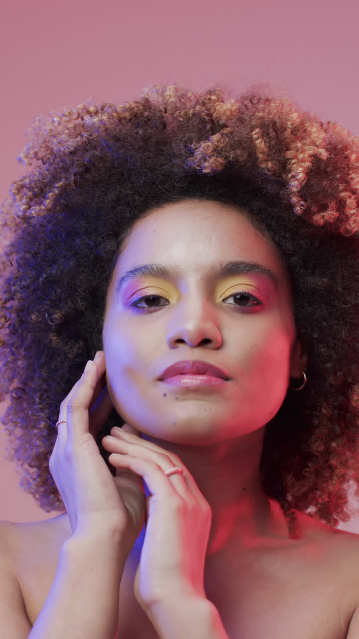 Vídeo vertical de mulher birracial com cabelo escuro em luz azul e rosa, em câmera lenta.