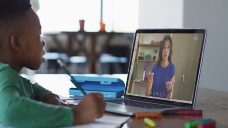 niño afroamericano sentado en un escritorio usando una computadora portátil teniendo una lección escolar en línea