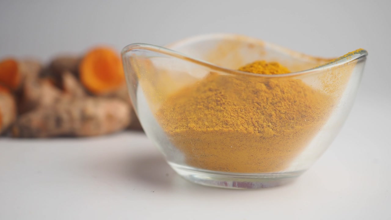 Bright Yellow Turmeric Powder in a Glass Bowl with Fresh Turmeric Roots