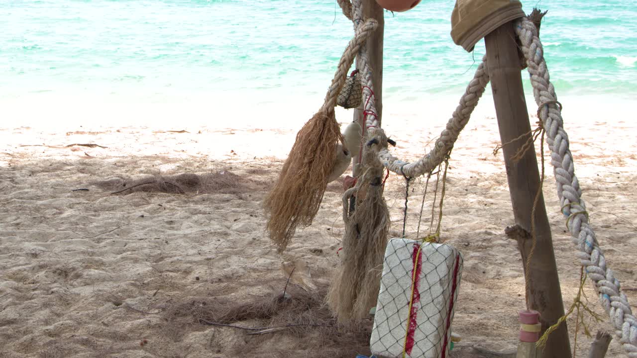 Inquadratura fissa a campo medio di cime da pesca e galleggianti in polistirolo appese su una soleggiata spiaggia tropicale.