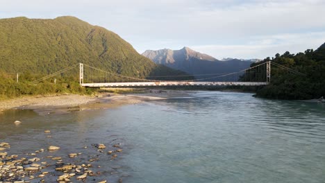 rusty old bridge crossing blue glacial stream before rugged mountains