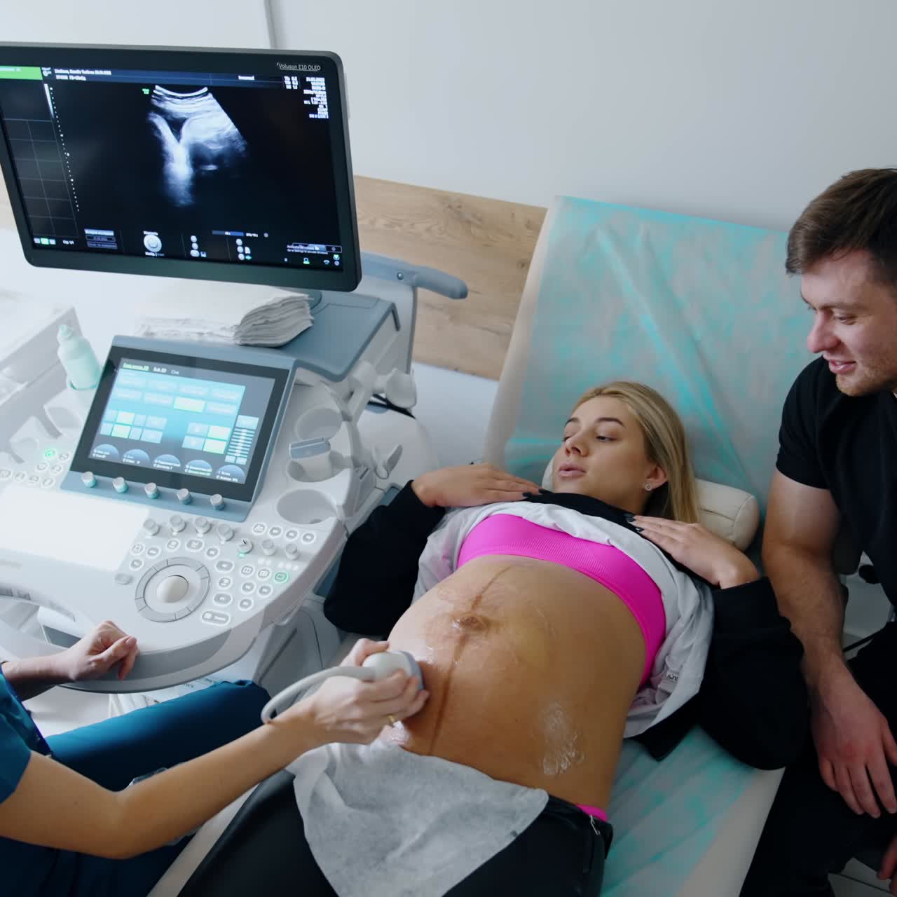 Obstetrician says something to a lady during the ultrasonic check up. Doctor looks at the monitor and explaining it to a patient