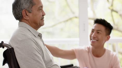 Diverse-male-physiotherapist-advising-and-senior-man-in-wheelchair-using-dumbbells,-in-slow-motion