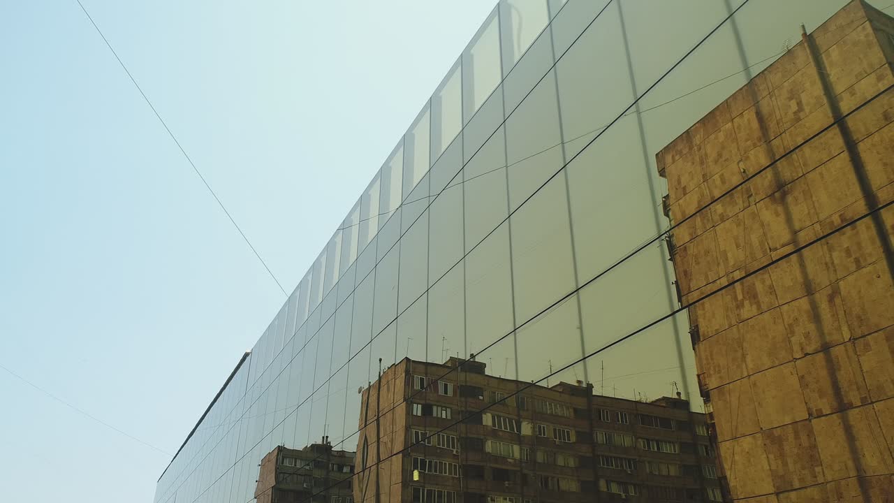 vista exterior de 4k de un edificio del distrito comercial o un centro comercial con ventanas de espejo de pared durante el día. luz solar. reflejo de la ciudad, coches y torres en paredes de espejo. cámara de avión no tripulado en movimiento