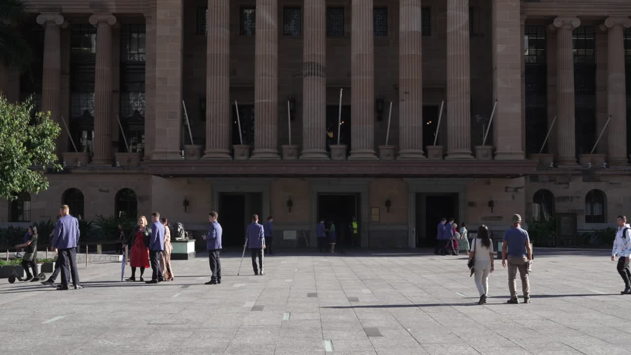 Pedestrians walking over square in Brisbane, Australia, with scenic architectural building in the background.