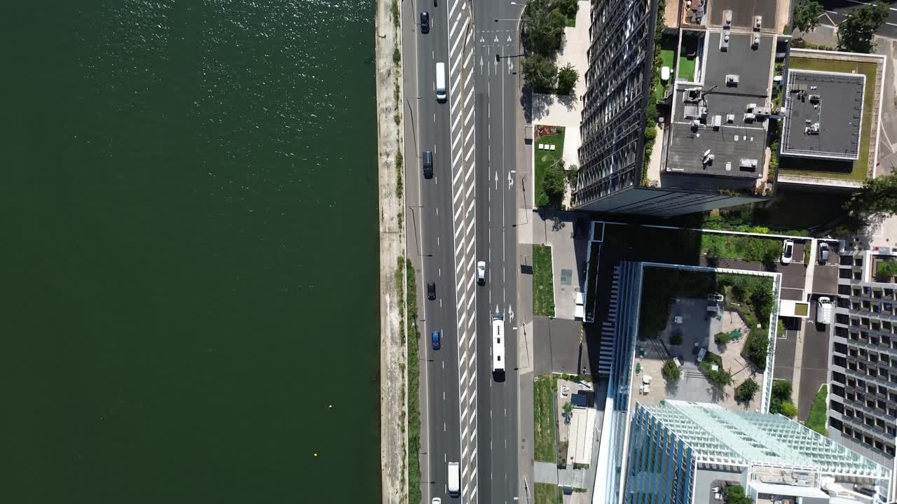 Carros circulando pela rua entre o Rio Sena e um bairro moderno de Paris na França.