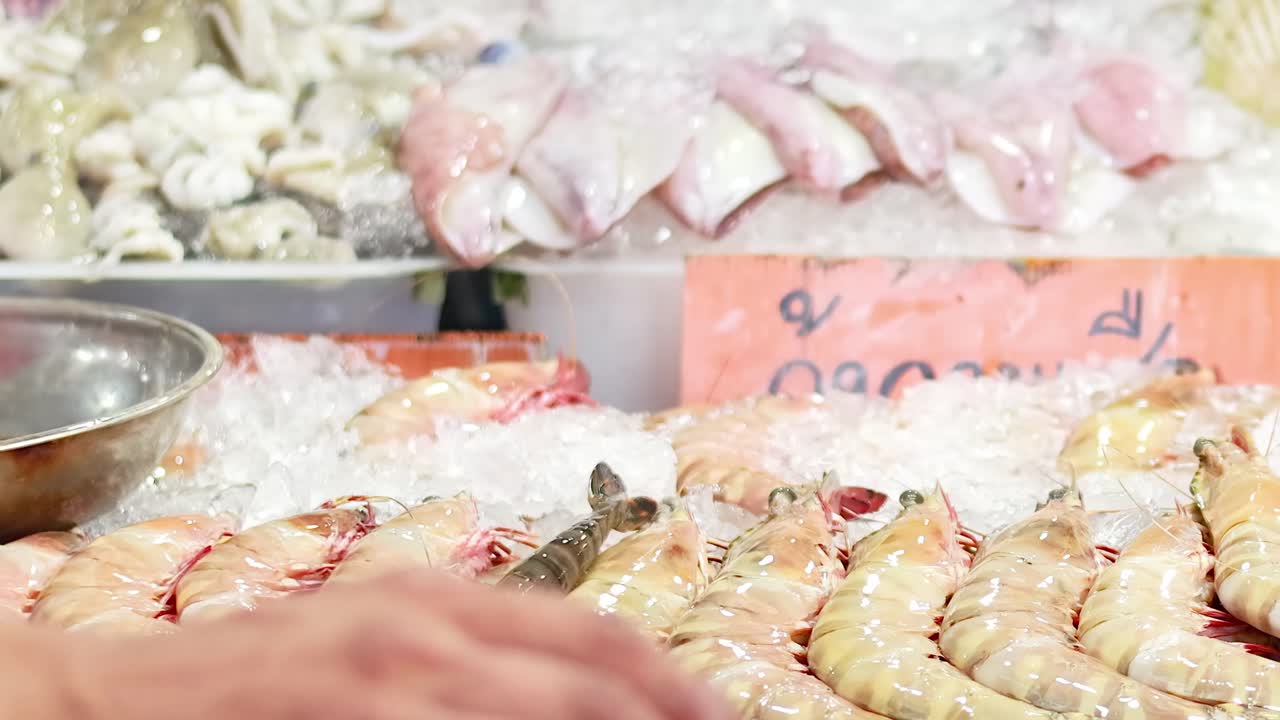 A vendor in a red jacket arranges shrimp on ice at a seafood market stall.