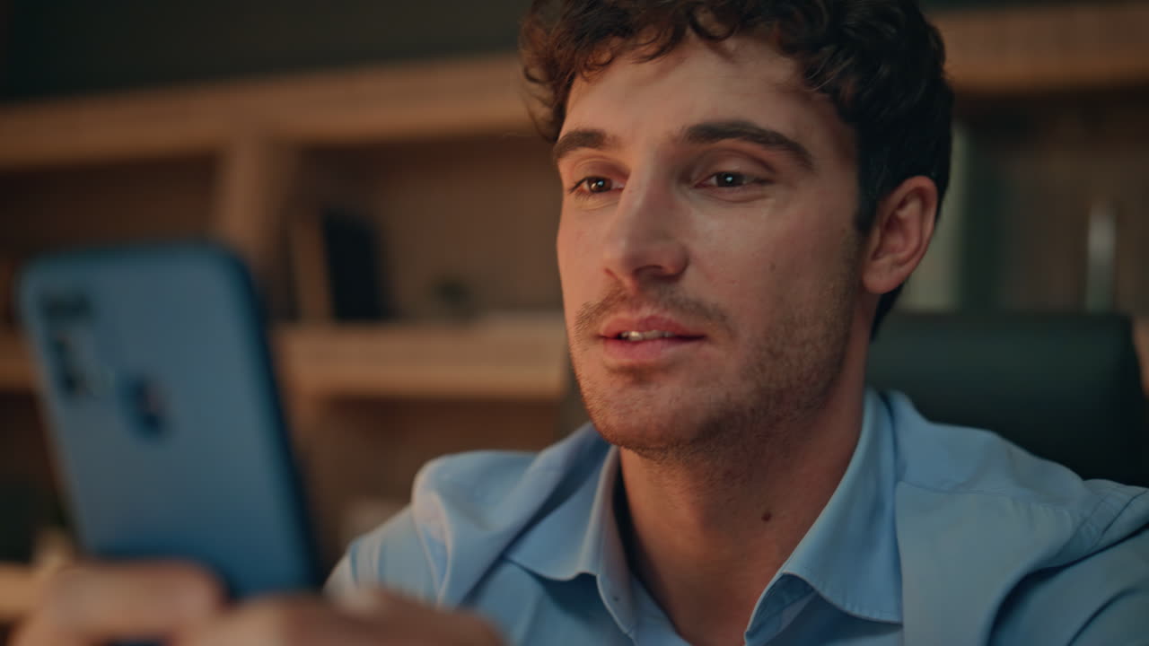 Smiling guy messaging smartphone at night home close up. Portrait cheerful man