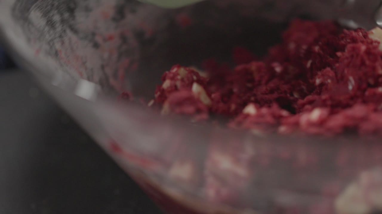 Primo piano di uno sbattitore elettrico che mescola impasto per biscotti red velvet in una ciotola di vetro