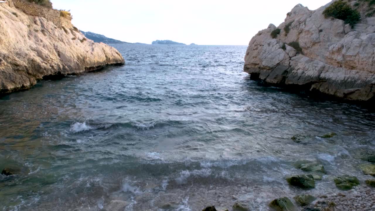 L'acqua si infrange tra le rocce frastagliate prima di riversarsi sulla piccola spiaggia di ciottoli di Marsiglia