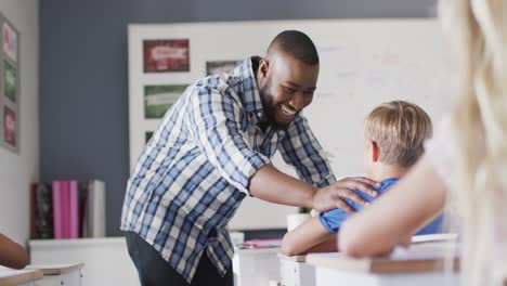 video of happy african american teacher supporting caucasian boy in classroom