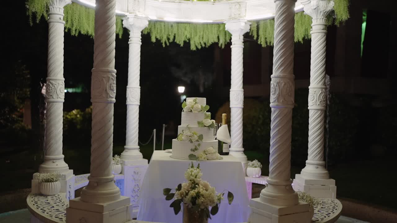 elegante pastel de bodas bajo un gazebo blanco adornado por la noche
