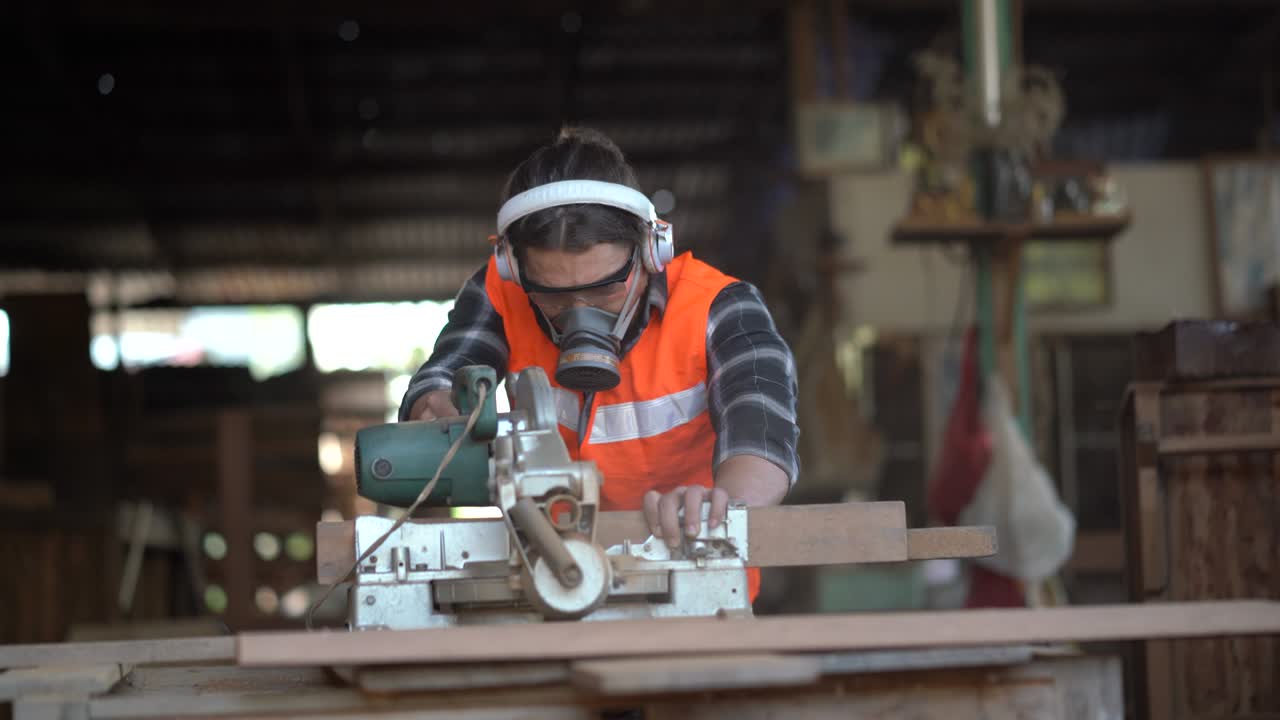 carpintero usando sierra circular cortando tabla de madera en el taller. joven constructor tabla de aserrar. artesano usando máscara de protección, protectores auditivos y gafas de seguridad.