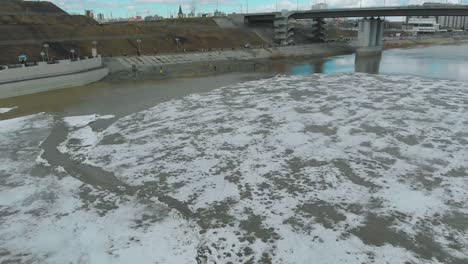 frozen-river-under-grey-bridge-against-city-buildings